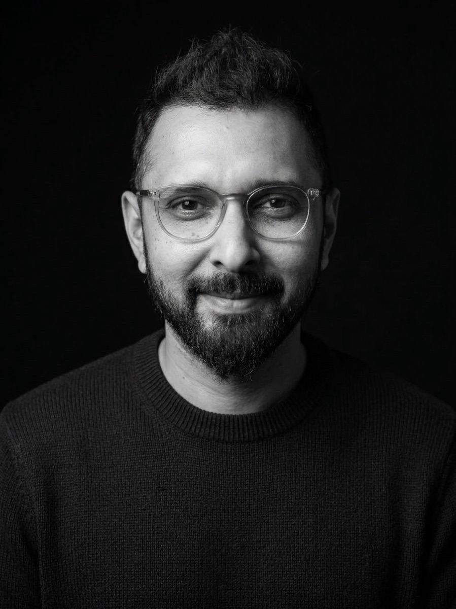 Diat Khan — black-and-white studio portrait against a dark background.